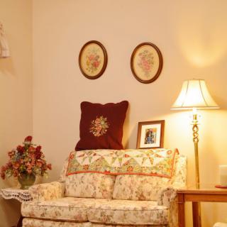 A cozy living room corner with a floral patterned sofa, a floor lamp, decorative wall art, and a vase of flowers.
