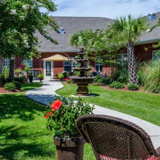 A serene garden with a fountain, lush greenery, and outdoor seating.