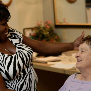 A caregiver interacts warmly with an elderly woman, sharing a moment of joy.