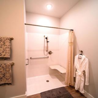 A modern bathroom with an accessible shower featuring a grab bar and foldable seat, complemented by a nearby towel rack and robe.
