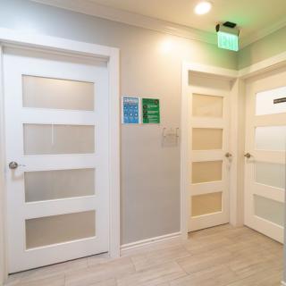 A modern hallway with white doors and an illuminated exit sign.