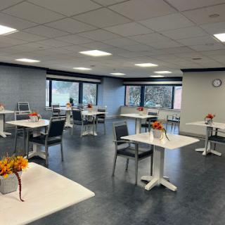 A spacious and modern dining area with well-arranged tables and floral decorations, illuminated by ample natural light.