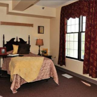 A cozy bedroom with a neatly made bed, decorative curtains, and a window allowing natural light to illuminate the room.