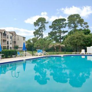 An outdoor swimming pool surrounded by apartment buildings and trees under a clear sky.