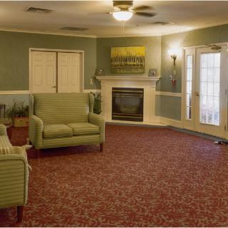 A cozy living room with green furniture, a fireplace, and red carpeting.