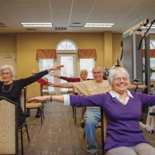 A group of seniors participating in a fitness class indoors, engaging in arm exercises.