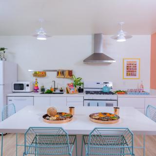 A modern kitchen with a clean white aesthetic featuring a dining table, chairs, and various appliances.