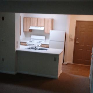 An apartment kitchen with a stove, refrigerator, and a view into the living area.