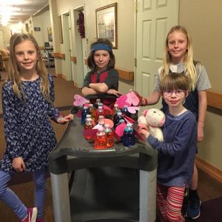 A group of children in a hallway with a cart full of toys.