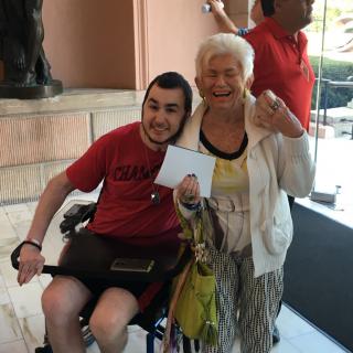 An elderly woman and a young man in a wheelchair share a joyful moment indoors.