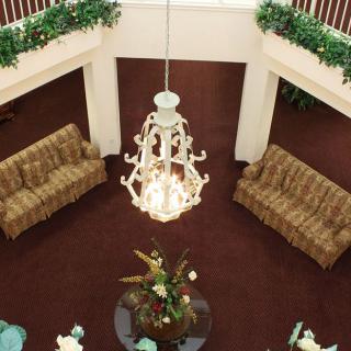 A spacious lobby with a central chandelier, surrounded by sofas and greenery.
