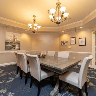 A well-appointed dining room featuring an elegant table, upholstered chairs, two chandeliers, and artwork on the walls.