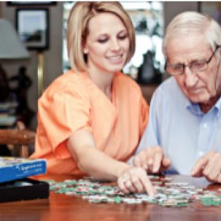 A caregiver assisting an elderly man with a puzzle at home.