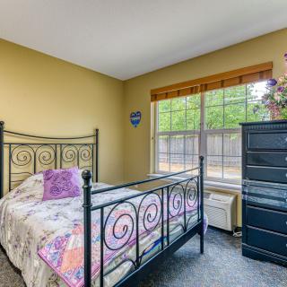 A cozy bedroom with a black metal bed frame, yellow walls, and ample natural light from a large window.