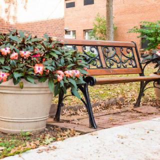 A quaint park bench adorned with potted flowers, set against a brick wall and sidewalk.