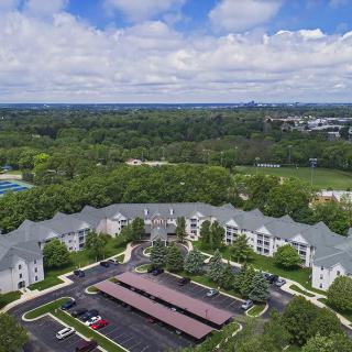 Aerial view of an apartment complex surrounded by lush greenery under a partly cloudy sky.