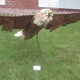 A metal sculpture of an eagle displayed on a lawn.