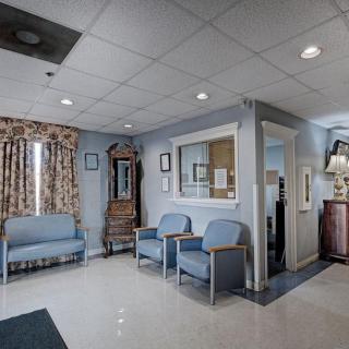A calm and well-lit waiting room featuring blue chairs and a grandfather clock.