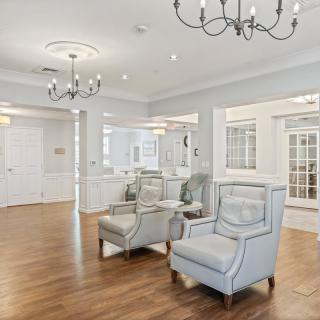 A spacious and elegantly designed living room featuring modern furniture, hardwood flooring, and bright lighting from chandeliers.