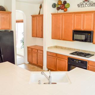 A bright kitchen featuring wooden cabinets, a countertop with a sink, and various appliances including a stove, microwave, and refrigerator.