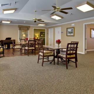 A spacious and well-lit room with several tables and chairs, ceiling fans, and a piano in the corner.