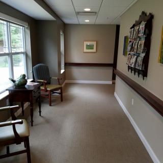 A quiet hallway with chairs and a window, adorned with pictures and carpeting.