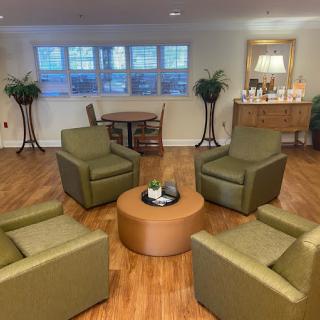 A cozy living room setup with four green armchairs arranged around a round coffee table, complemented by potted plants and warm lighting.