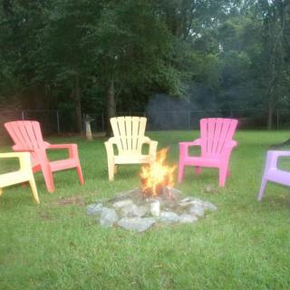 Colorful chairs arranged around a fire pit in a grassy backyard setting.