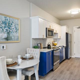 A modern kitchen with blue and white cabinetry, a dining table, stylish decor, and stainless steel appliances.