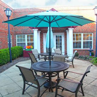 A cozy outdoor patio setup with a large umbrella and seating arrangement in front of a brick building.