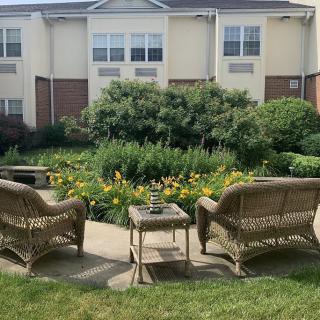 A cozy outdoor patio with wicker chairs overlooking a lush garden in front of a residential building.