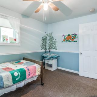 A cozy children's bedroom with a colorful quilt on a twin bed, featuring cheerful wall art and a ceiling fan.