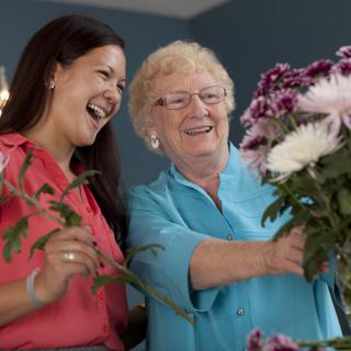 Two women happily arranging flowers together indoors.