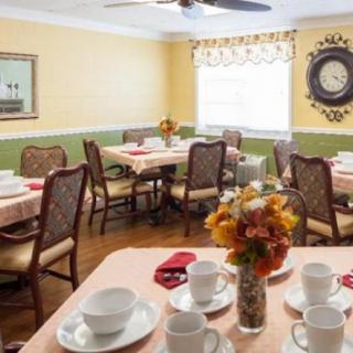 A cozy dining room with neatly arranged tables and chairs, featuring floral centerpieces and a warm color scheme.