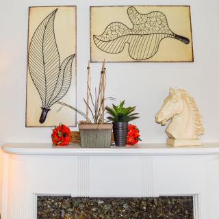 A well-decorated mantel featuring modern leaf artwork, a small plant arrangement, and a horse head sculpture.