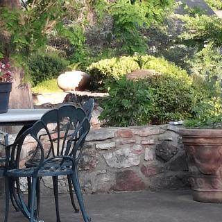 A tranquil patio area with outdoor seating surrounded by lush greenery and a stone wall.