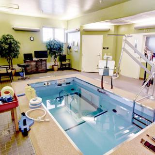 A spacious indoor therapy pool equipped with various exercise tools and a lift for rehabilitation purposes.