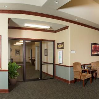 A hallway with seating area, featuring chairs and a table next to wall art and a plant.