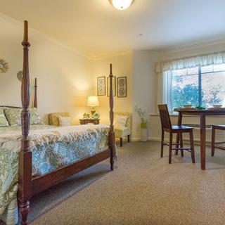 A cozy bedroom with a four-poster bed, featuring elegant decor and a small table by the window.