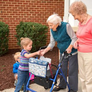 A heartwarming interaction between children and elderly women outdoors near a brick wall.