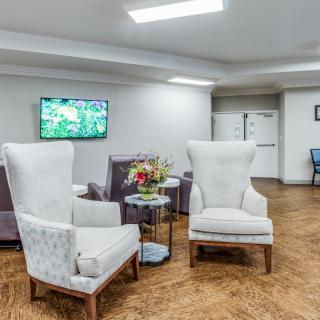 A modern living room with armchairs, a small table with flowers, and a wall-mounted television.