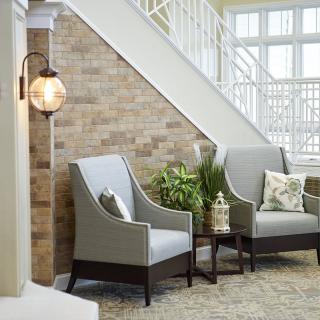 A cozy living area with two armchairs, a side table, and decorative plants against a brick wall near a staircase.