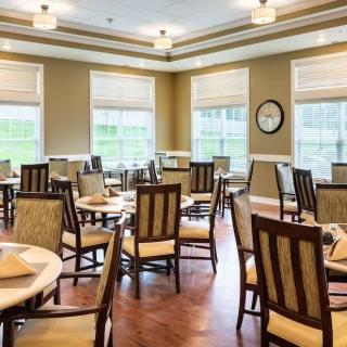 A well-lit dining room with multiple tables and chairs, featuring large windows and modern decor.