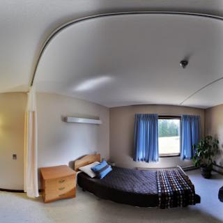 A panoramic view of a cozy bedroom featuring a bed, bedside table, and bright window.