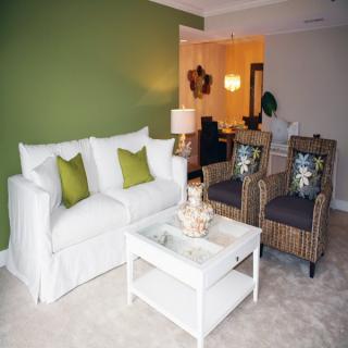 A modern living room with a white sofa, green accent wall, and stylish decor.