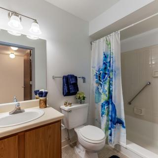 A clean and modern bathroom with a sink, mirror, toilet, and shower with a colorful curtain.