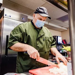 A chef is chopping ingredients on a red cutting board in a professional kitchen.