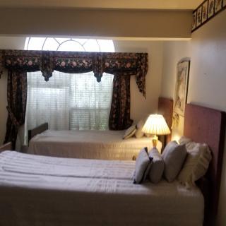 A cozy bedroom with two beds, a lamp, and a window with decorative curtains.