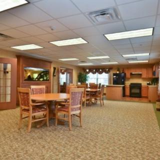 A cozy dining area with wooden tables and chairs, carpet flooring, and ceiling tiles.