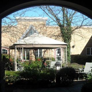 A view through an archway of a courtyard featuring a gazebo surrounded by outdoor seating and greenery on a sunny day.